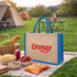 A coloured jute tote bag in natural and blue with a logo, placed on a picnic blanket beside food and drinks.