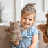 A plush hippopotamus hand puppet in brown, held by a smiling child wearing a blue dress, with a decorative headband.