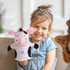 A cow hand puppet with pink ears and black patches, held by a smiling child wearing a blue dress.