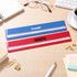 A blue and red dual scale 30CM magnifying ruler with a logo, placed on a wooden desk alongside office supplies.