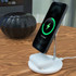 A white 2-in-1 wireless charger with a phone and earbuds charging, set on a wooden table.