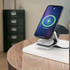 A silver and black foldable wireless charger stand, with a phone and AirPods charging on a wooden table.