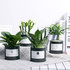 Four small black tin cans without lids, each containing different types of artificial plants in various shades of green.