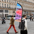 A backpack with a black base and a colourful feather flag attached, prominently displaying a promotional message.