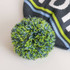 A grey beanie with a light blue and green striped pattern, featuring a colourful pom-pom on top.