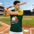 A men's 100% polyester sublimated baseball jersey in green and yellow, featuring a logo, worn by a model holding a bat.