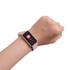 A pink square smart band worn on a wrist, displaying health metrics on its screen. The device has a logo.