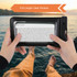A waterproof phone bag with a full-length clear window, black in colour, held by two hands against a scenic background.