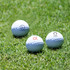 Three white golf balls on green grass, featuring logos on the surface of each ball.