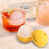 A yellow silicone whisky ice ball mould next to a glass of cocktail featuring an ice ball and garnished drink.
