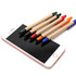 A collection of stylus pens in red, blue, green, and black lined up against a smartphone screen. Each pen has a paper barrel and a touch head.