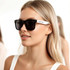 Stylish black sunglasses with white arms, featuring a logo, worn by a woman with long blonde hair.