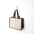 A functional tote bag in beige and black hangs on a blue hook against a white wall. The bag has handles and a logo.