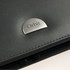 A black leather zippered compendium featuring a branded metal accent.
