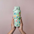 A drink bottle in mint green featuring various colourful designs and a lid with a handle. It includes a logo.