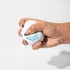 A white squeeze ball is being held, featuring a blue logo. The ball is shown being squeezed by a hand.