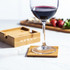 A bamboo coaster sits on a marble surface under a wine glass, alongside a wooden tray with strawberries and salad.