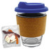 A glass coffee cup with a cork band and blue lid, accompanied by a bag of mixed lollies in various colours.