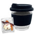 A clear glass coffee cup with a black lid and sleeve, beside a packet of mixed jelly lollies in various colours.