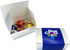 A white box containing four assorted chocolate balls, featuring vibrant red, yellow, and blue wrappers, with a branded outer sleeve.