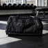 A black duffle bag with multiple zippered compartments and a logo, resting on a gym floor.
