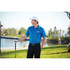A blue short sleeve polo shirt for men, featuring a logo, worn with black trousers near a scenic outdoor setting.