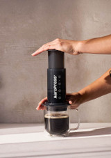 a hand applying pressure to the AeroPress Coffee Maker , with coffee pouring into a glass cup