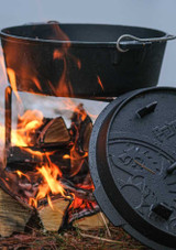 Petromax Dutch Oven FT6-T – 5.5 L flat-base cast-iron pot with raised-edge lid, shown in use cooking on ambers.