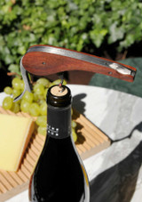L’Atelier du Vin Soft Machine Rosewood – single-motion gear corkscrew with polished rosewood body, integrated foil cutter and bottle opener, shown in use on a bottle of wine