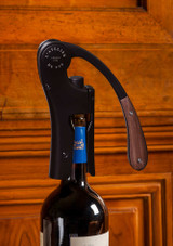 L’Atelier du Vin Oeno Motion Wood & Black – vertical lever corkscrew with black metal body and dark wood handle, shown in use on a bottle of wine