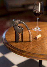 L’Atelier du Vin Oeno Motion Wood & Black – vertical lever corkscrew with black metal body and dark wood handle, shown on a table L’Atelier du Vin Oeno Motion Wood & Black – vertical lever corkscrew with black metal body and dark wood handle, shown on a table