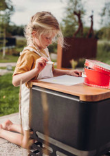 A girl colouring outdoors using the Höfats CUBE Board as a table.