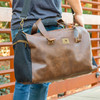 Danville Duffel with Watkins Wellness logo being held in front of a brick wall.