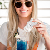 Beautiful young woman infusing her cocktail with Ahya's Calm Lavender Chamomile beverage infusion