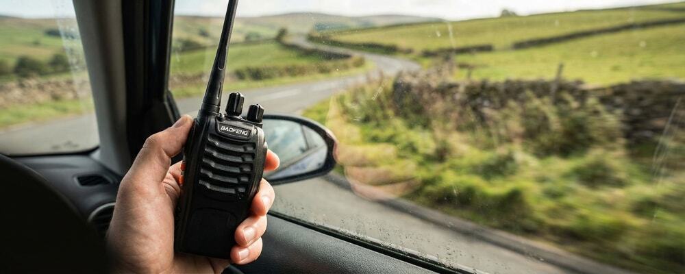 Passenger using a Baofeng walkie talkie near the car window to maximize range