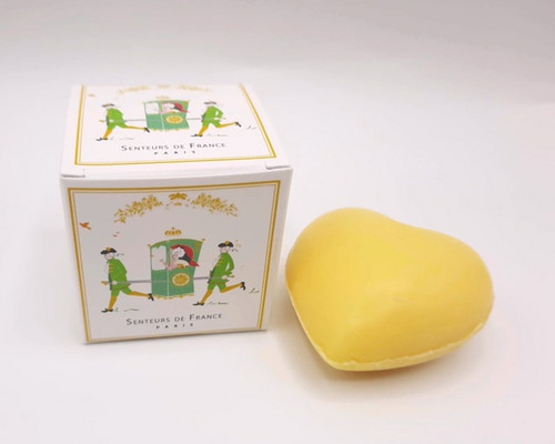A box containing a 20 gram heart-shaped mini honysuckle soap bar from Senteurs de France. The yellow soap heart sits next to its box, which features a cartoon of two people carrying Marie-Antoinette on a sedan chair.