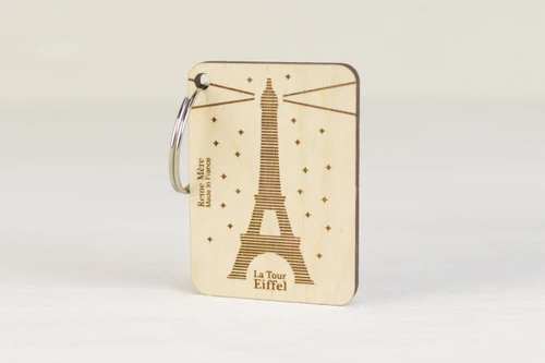 A key ring with a square wooden charm. The charm is has an illustration of the Eiffel Tower, illuminating the surrounding area.
