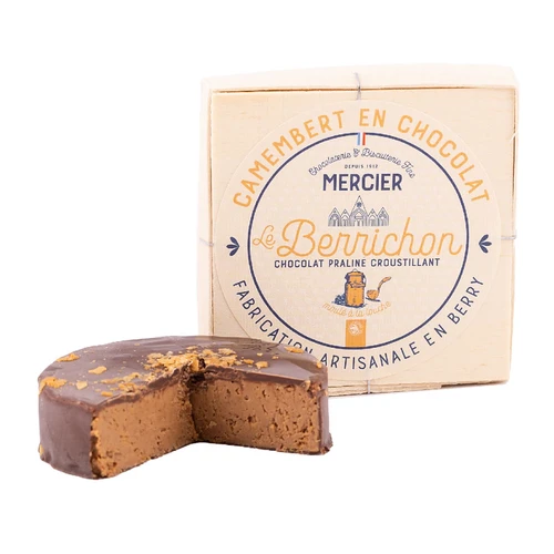 A wooden box from Mercier containing 100 gram mini chocolate praliné "Camambert." In front is the chocolate, which is shaped like a cheese wheel and has a wedge taken out to reveal the praliné filling.