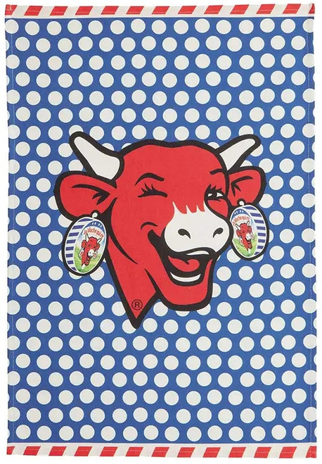 A "Coucke Vache Qui Rit" tea towel. In the center is an image of the red iconic "laughing cow," surrounded by white polka dots on a blue background.