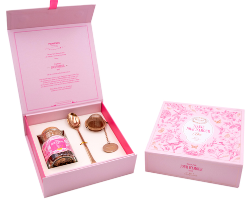 A pink case containing a glass jar of Provence d'Antan organic herbal tea, a tea infuser, and a spoon. The case is labeled "Jour d'Amour" and its border features sketches of flowers and birds.