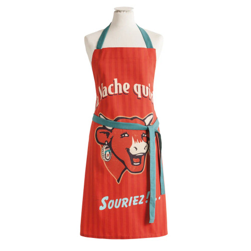 A red "Vache Qui Rit" (Laughing Cow) apron from Coucke. In the center is the iconic laughing cow, a red cow with horns and an earring. She says, "Souriez!"