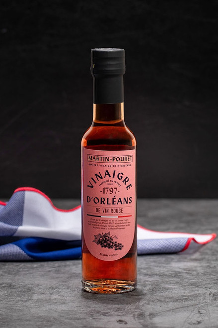 A 25 centiliter glass bottle from Martin-Pouret containing Orléans red wine vinegar. The bottle sits on a stone countertop with a French flag behind it.
