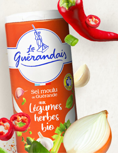 A red-orange canister containing 250 grams of Le Guérandais fine sea salt with organic vegetables and herbs being tossed alongside onions and peppers.