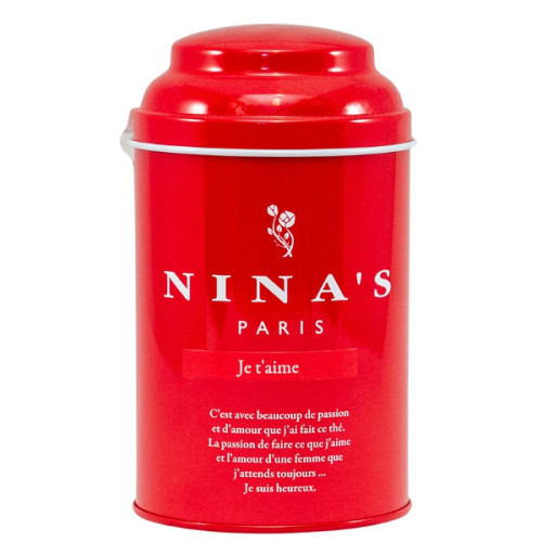 A crimson red round tin containing 100 grams of "Je T'aime" loose leaf tea from Nina's Paris. The tin has a simple design, and the bottom inscription reads in plain text, "C'est avec beaucoup de passion et d'amour que j'ai fait ce thé. La passion de faire ce que j'aime et l'amour d'une femme que j'attends toujours... Je suis heureux."