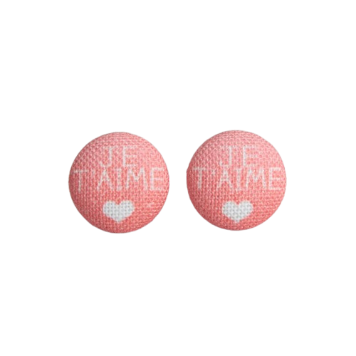 Two pink fabric button earrings with white text that says, "Je t'aime," followed by a white heart, from Rachel O's.