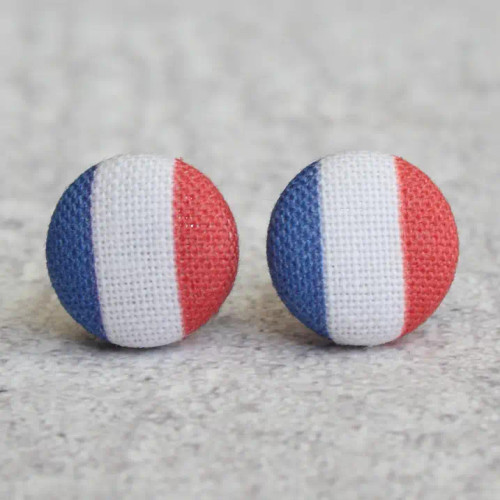 A pair of fabric button earrings colored like the French flag from Rachel O's. The earrings are on a gray stone counter top.