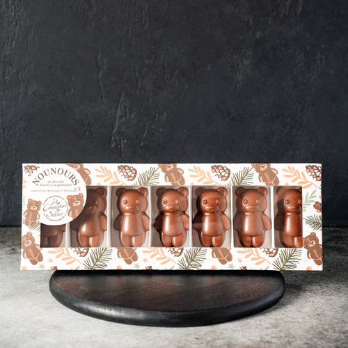 A 110 gram box of marshmallows covered in milk and dark chocolate, shaped into bears. From Le Chocolatier Sablais. The box is on a wooden coaster on a stone countertop.