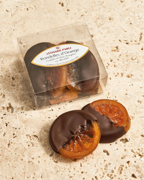 A box of 100 grams of candied orange slices, dipped in dark chocolate, from Léonard Parli. The box is displayed on a stone countertop.