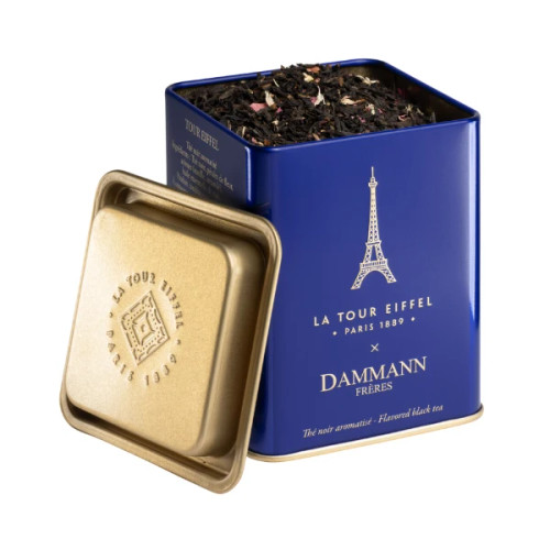A royal blue tea tin with its lid off to the side,  with visible black tea in the tin. Dammann Frères' golden Eiffel tower logo features prominently on the front of the tin.