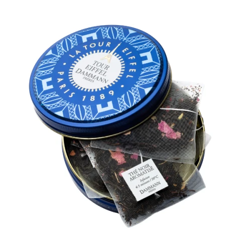 A royal blue tea tin with its lid off to the side,  with visible black tea bags in the tin. Dammann Frères' golden Eiffel tower logo features prominently on the front of the tin.